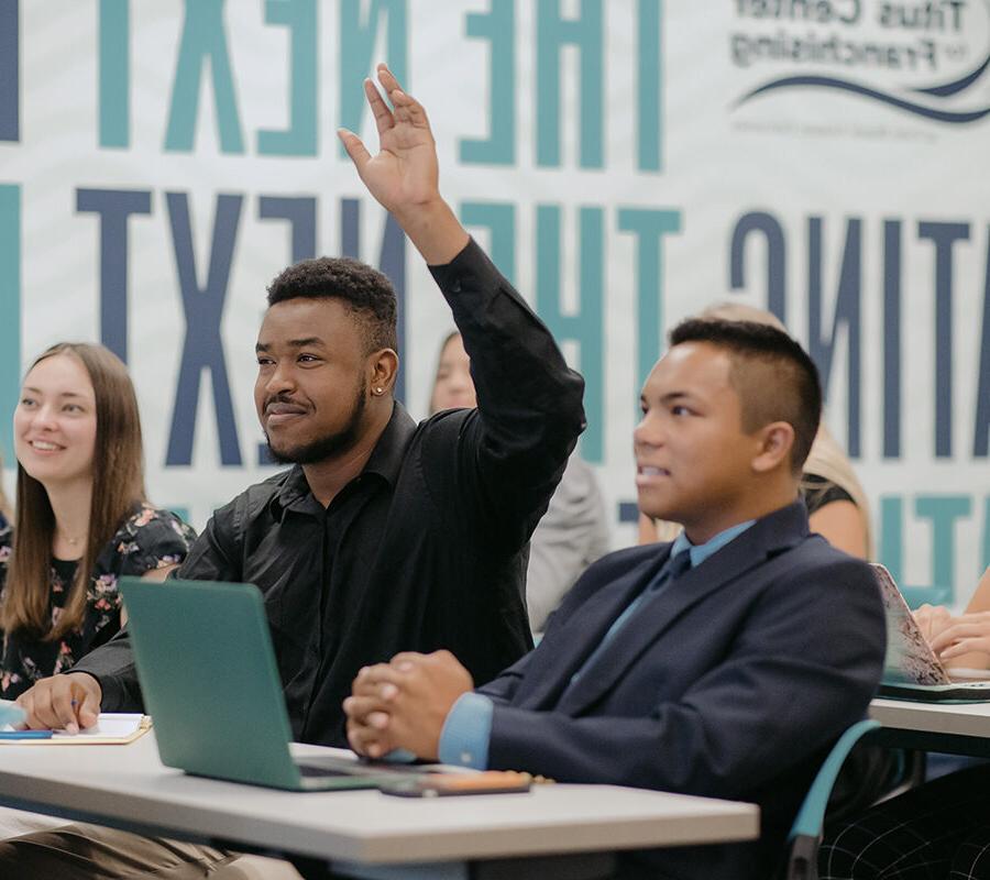 Student raises his hand in classroom lecture.